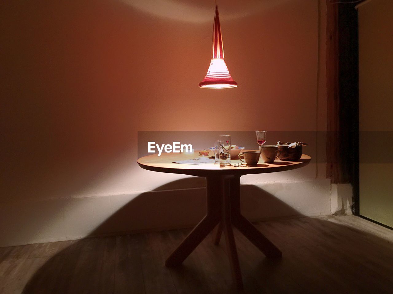 Illuminated pendant light above drinking glasses and cups served with food on table