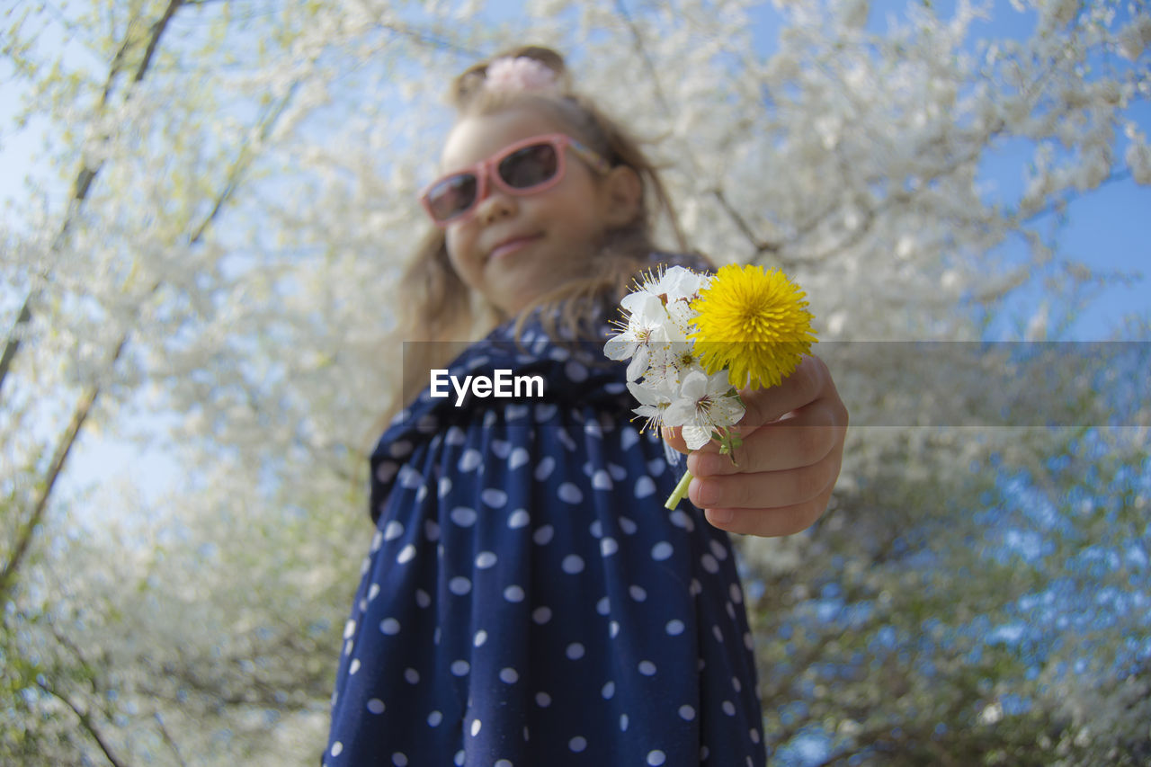 Low angle view of girl holding flowers while wearing sunglasses at park