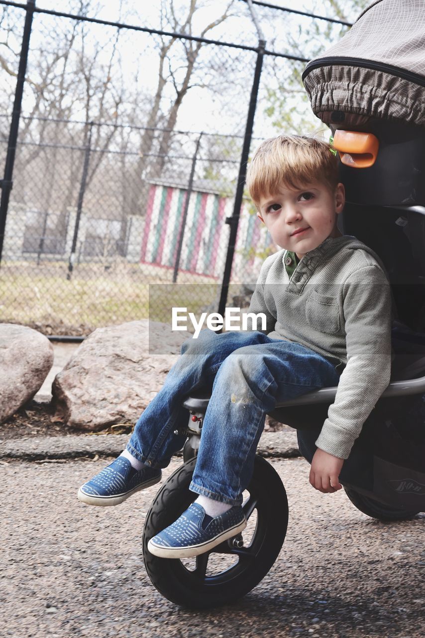 Cute boy sitting in baby stroller at park