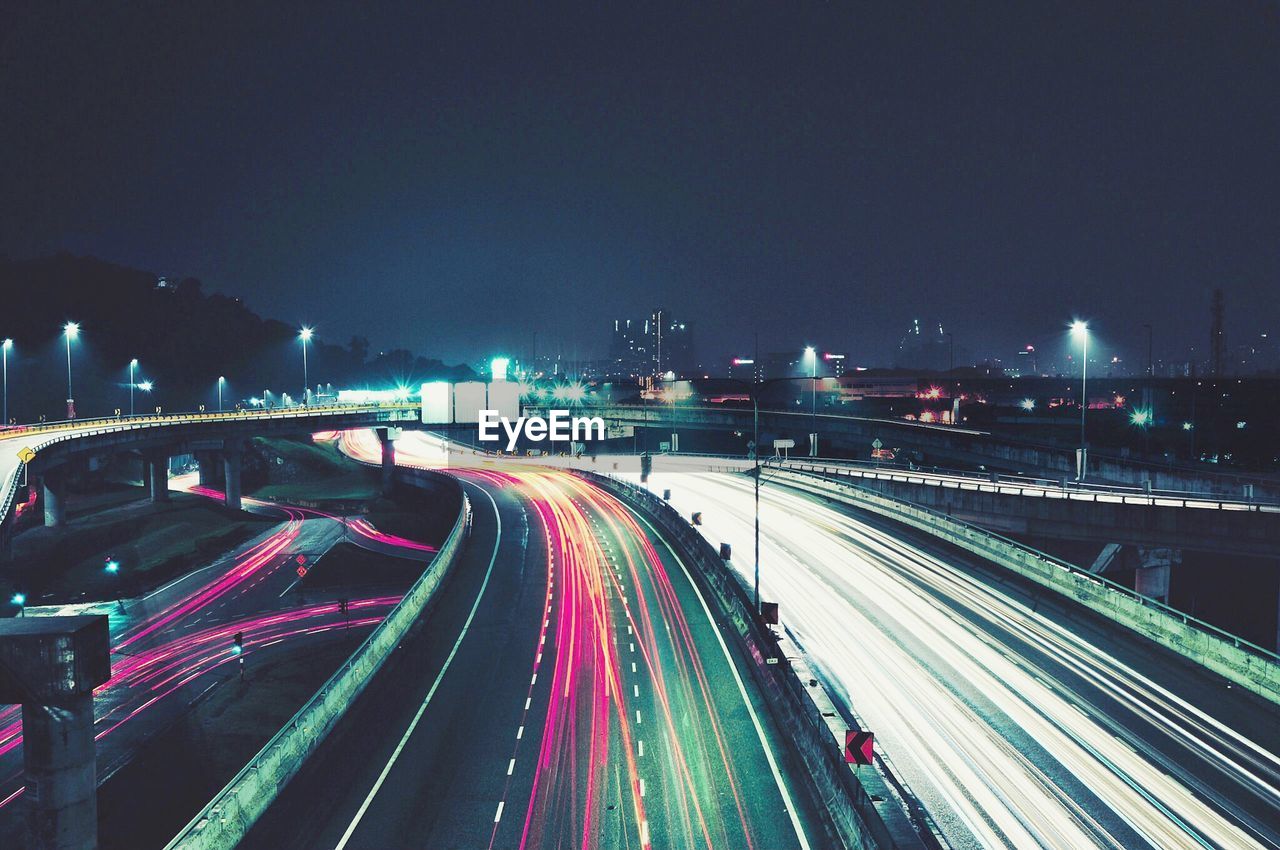 Illuminated light trails on highway in city against sky at night