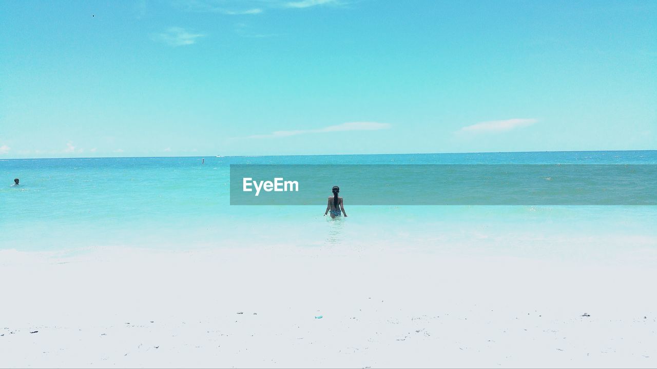 Rear view of girl in sea against blue sky