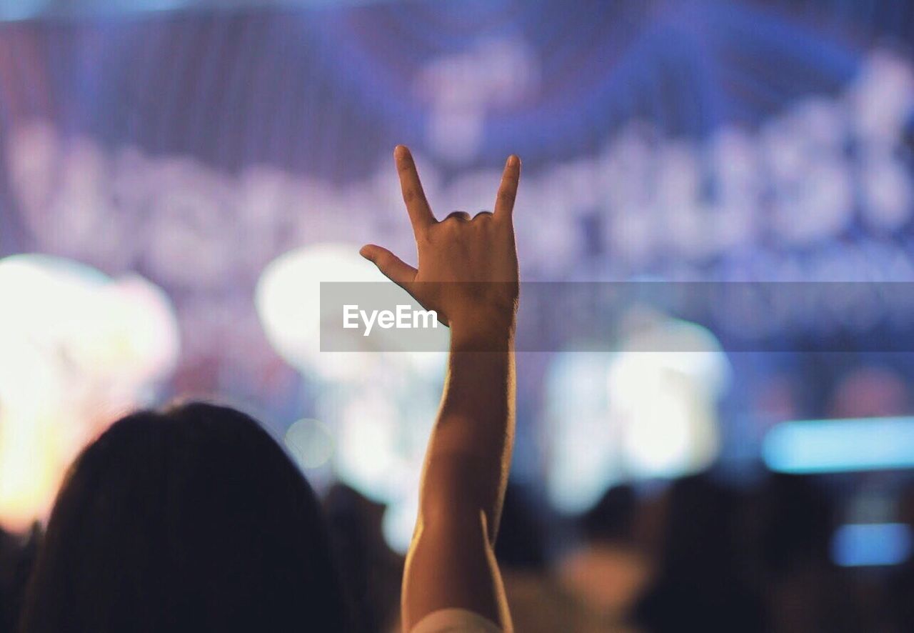 Cropped hand showing horn sign against blurred background