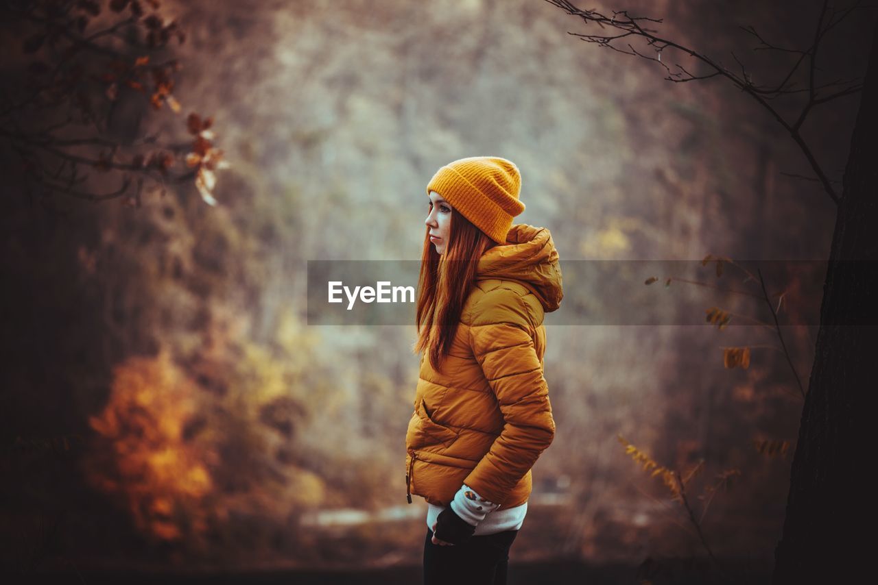 Side view of young woman standing in forest during autumn