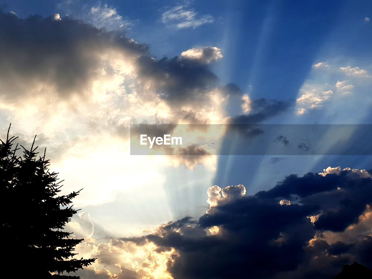 LOW ANGLE VIEW OF SUN STREAMING THROUGH CLOUDS IN SKY