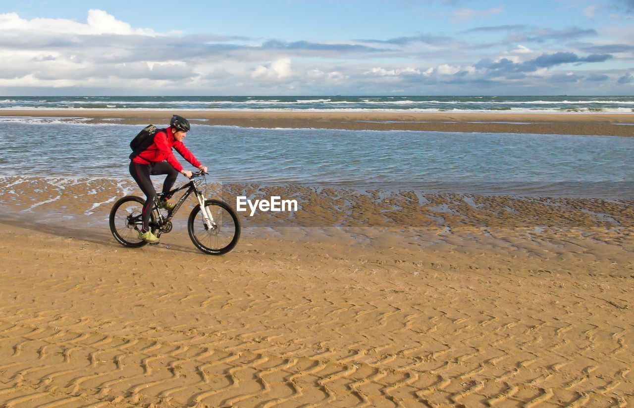 MAN RIDING BICYCLE ON SHORE