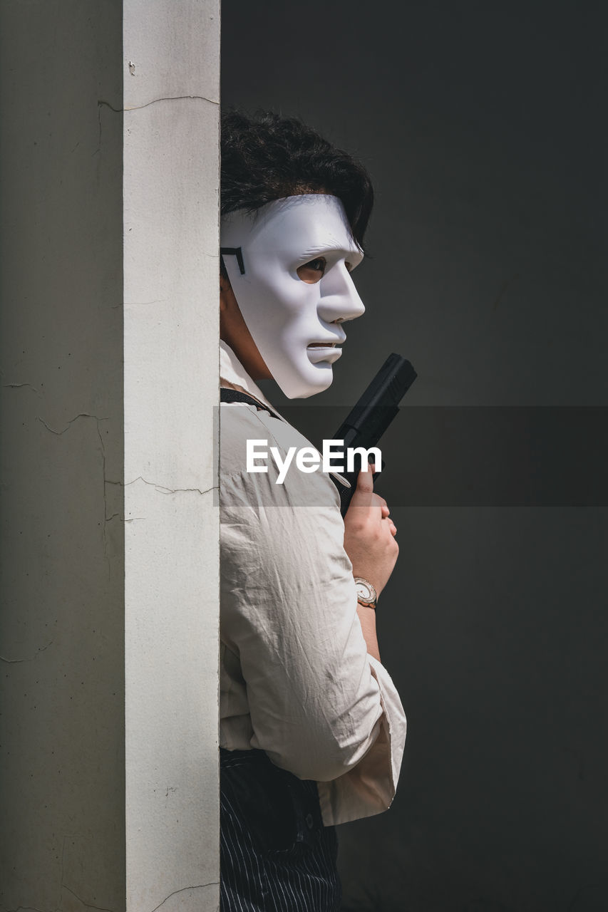 Portrait of a person wearing a mask holding up a fake gun behind a wall
