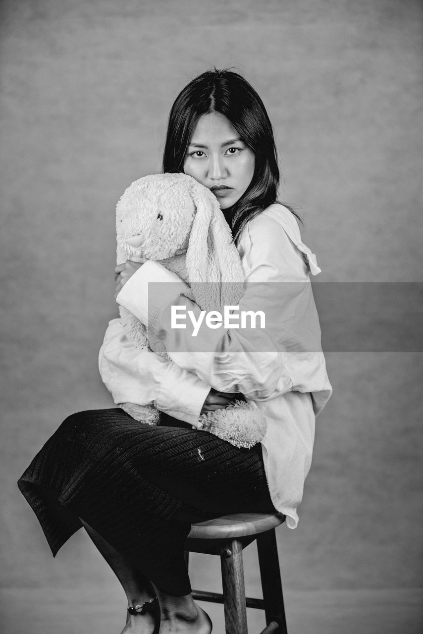 Emotional portrait of woman sitting on chair with stuffed toy