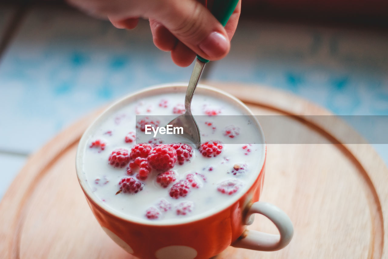 Close-up of hand stirring milk and berries in cup