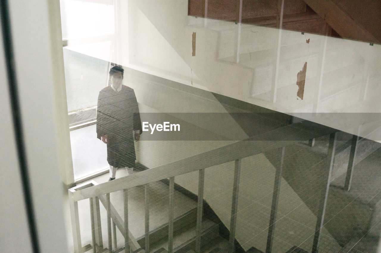 Portrait of man in graduation gown standing on stairs in building