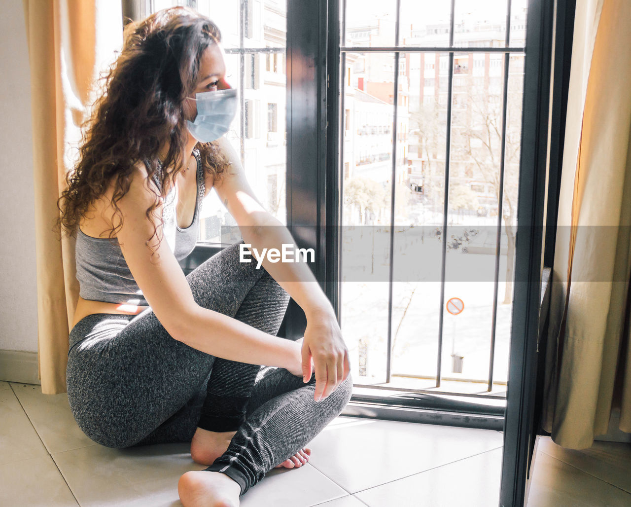 Young girl confinement with face mask at home looking out the window