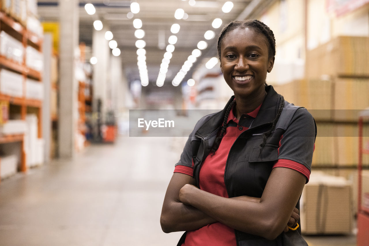 Smiling saleswoman with arms crossed standing in warehouse at hardware store