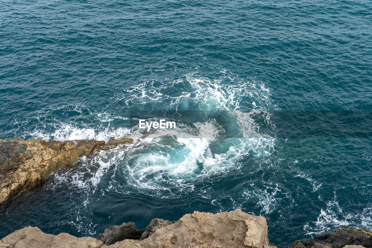 HIGH ANGLE VIEW OF WAVES BREAKING ON ROCK