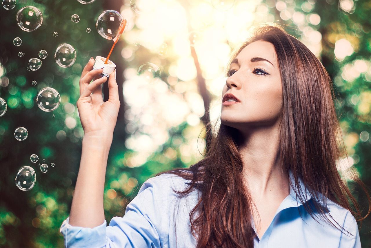 Beautiful woman holding bubble wand against trees