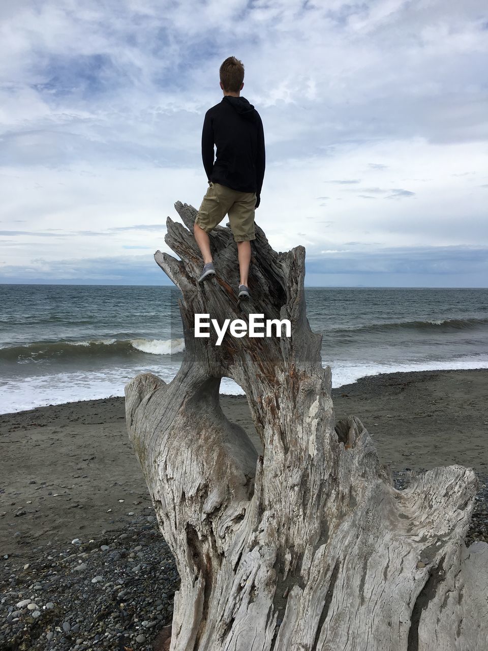 REAR VIEW OF MAN STANDING AT BEACH