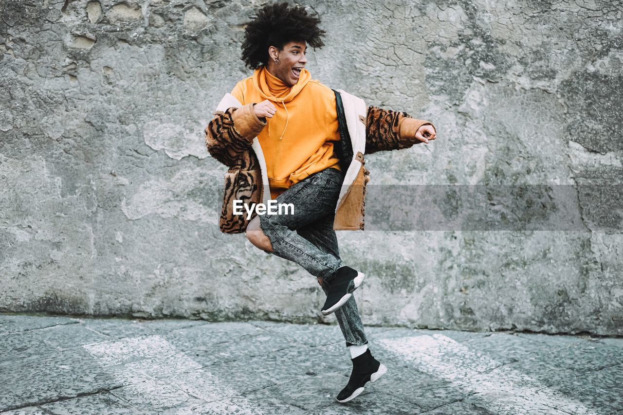 Cheerful young man looking away while running against wall