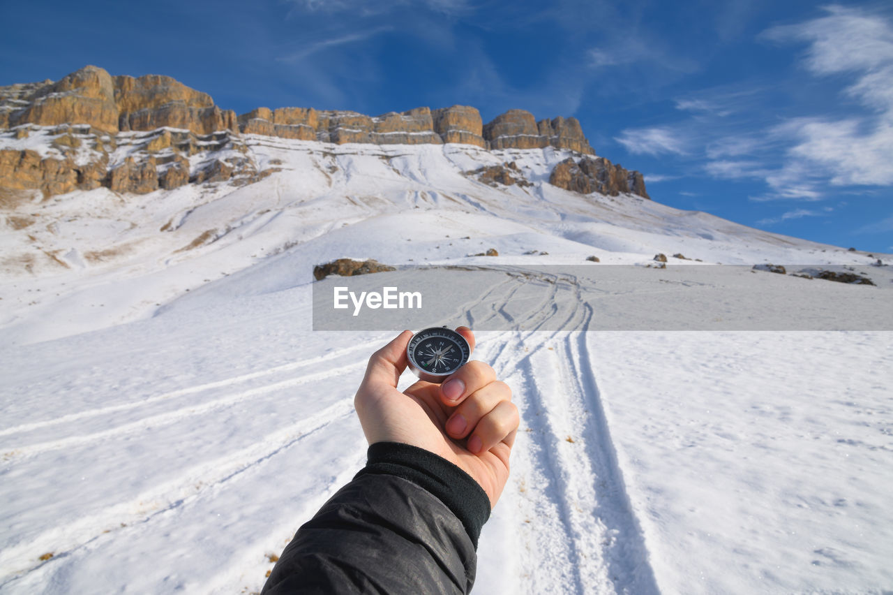 A man's hand holds a pocket magnetic compass for navigation against the backdrop of a rocky slope  