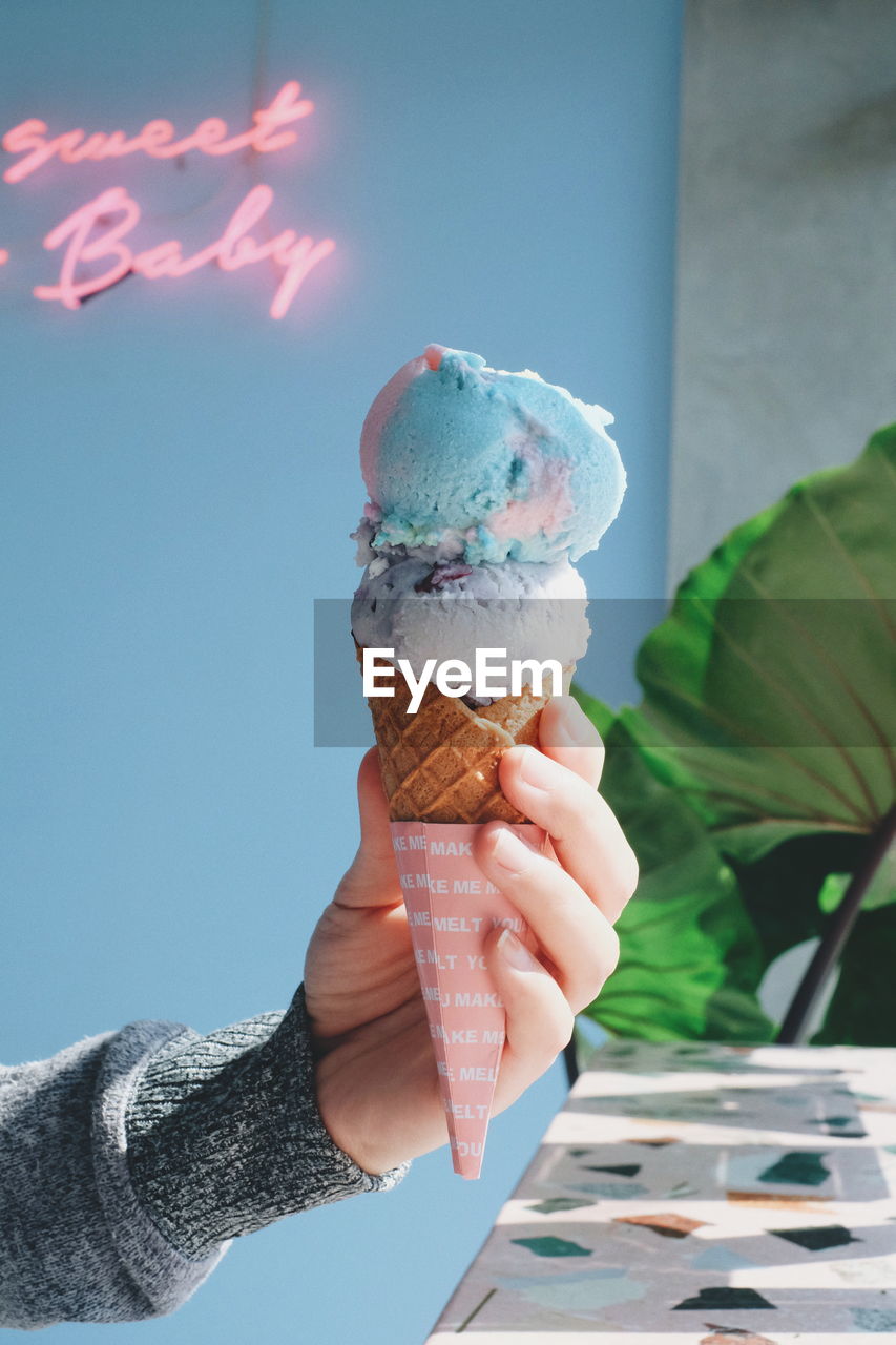 PERSON HOLDING ICE CREAM CONE AGAINST BLUE SKY