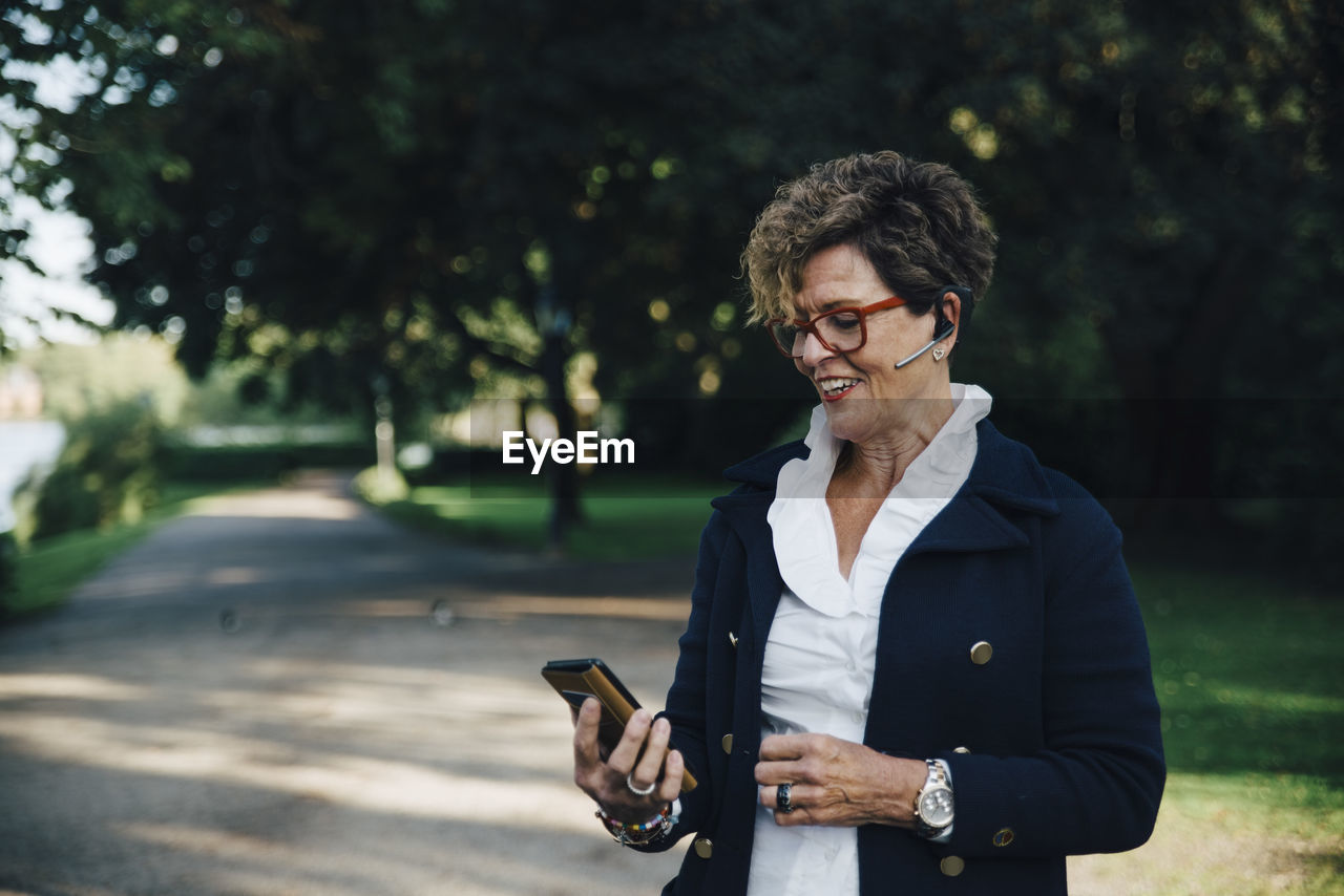 Senior woman wearing hands free device while using mobile phone in park
