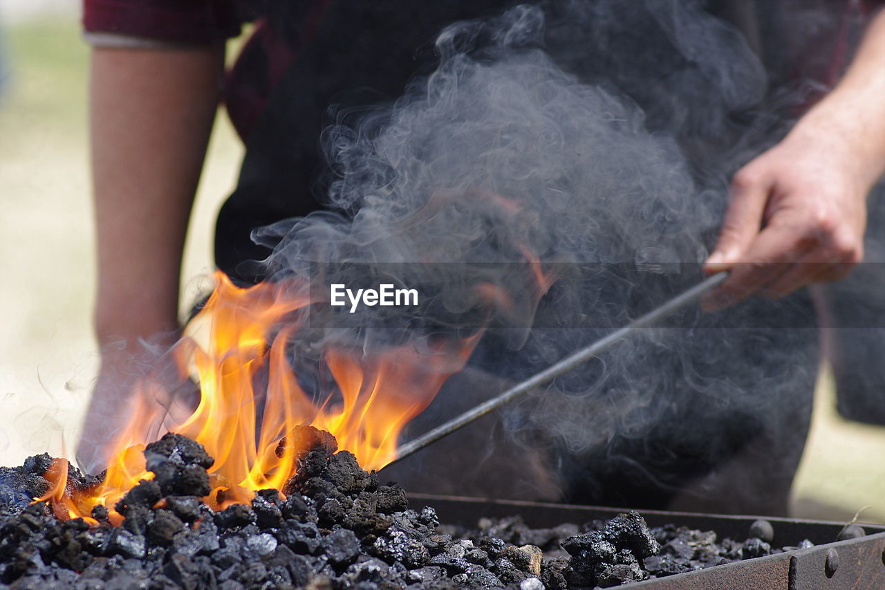 Midsection of man burning coal in barbecue