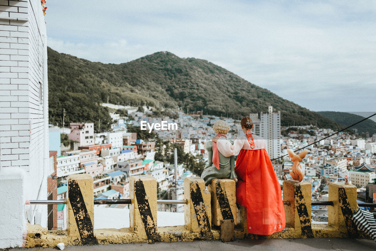 REAR VIEW OF PERSON AGAINST BUILDINGS ON MOUNTAIN