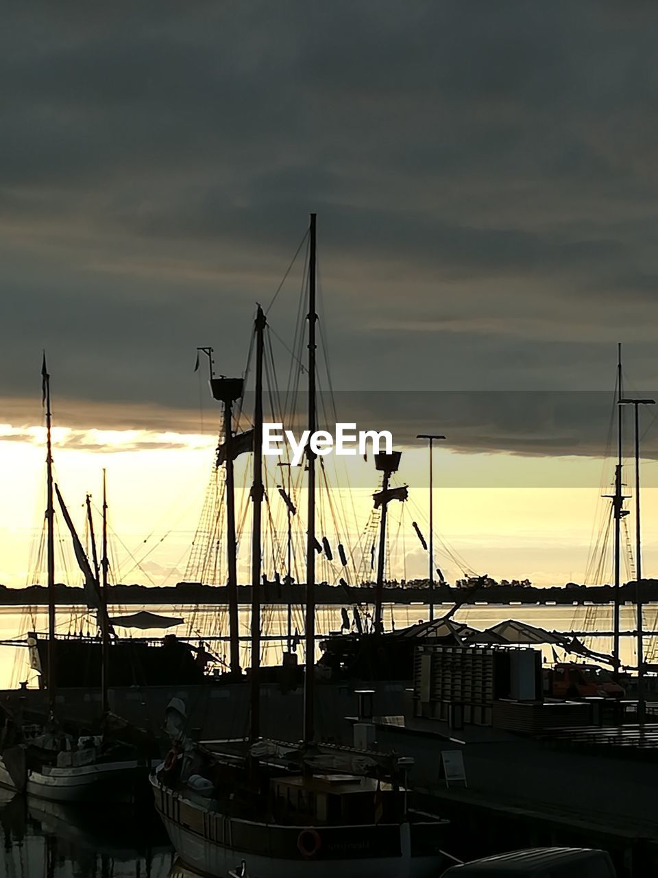 SAILBOATS MOORED AT HARBOR DURING SUNSET