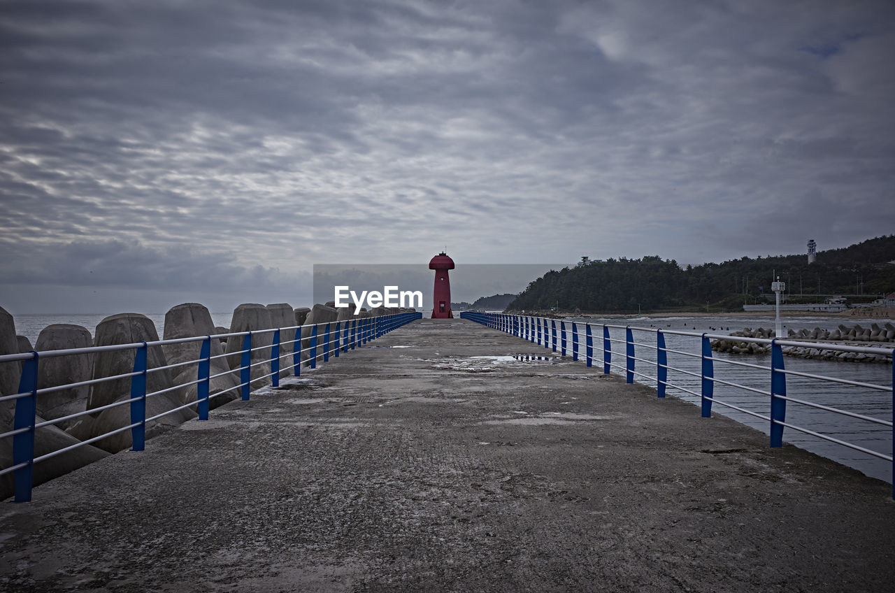 REAR VIEW OF WOMAN STANDING BY RAILING AGAINST SKY