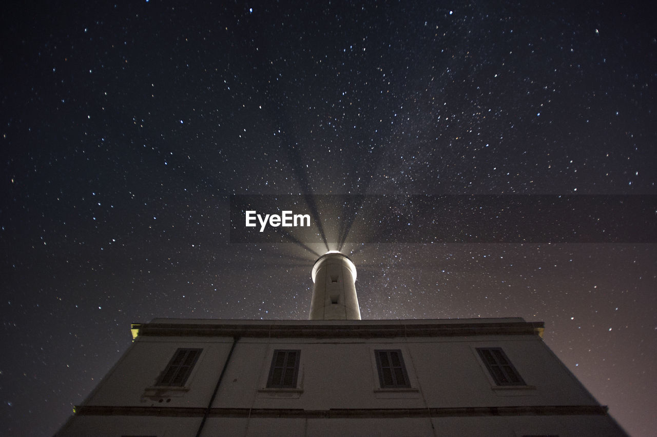 Low angle view of illuminated lighthouse against sky at night