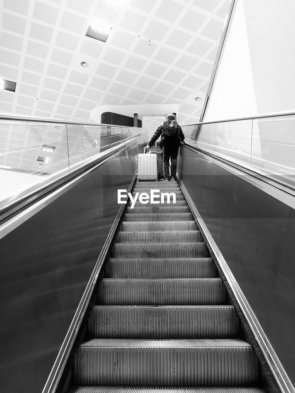 Low angle view of man with luggage standing on escalator