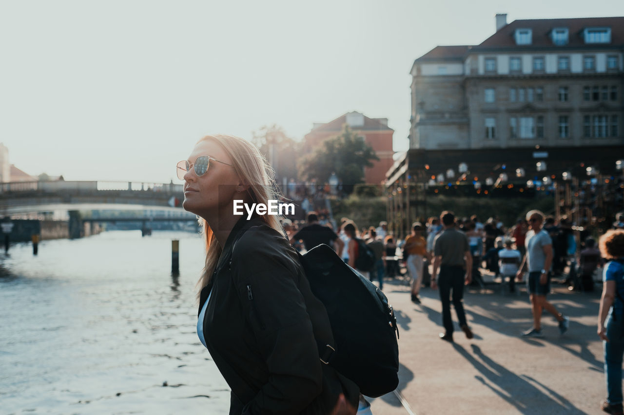 Young woman looking away while standing in city against sky