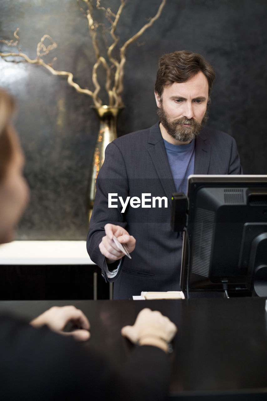 Male receptionist accepting payment through credit card from customer in hotel