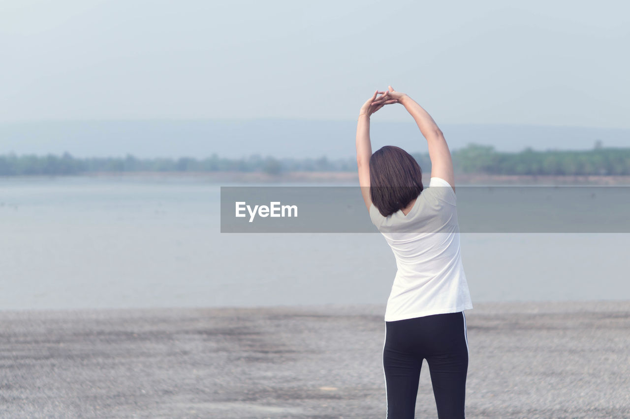 REAR VIEW OF WOMAN STANDING BY WATER