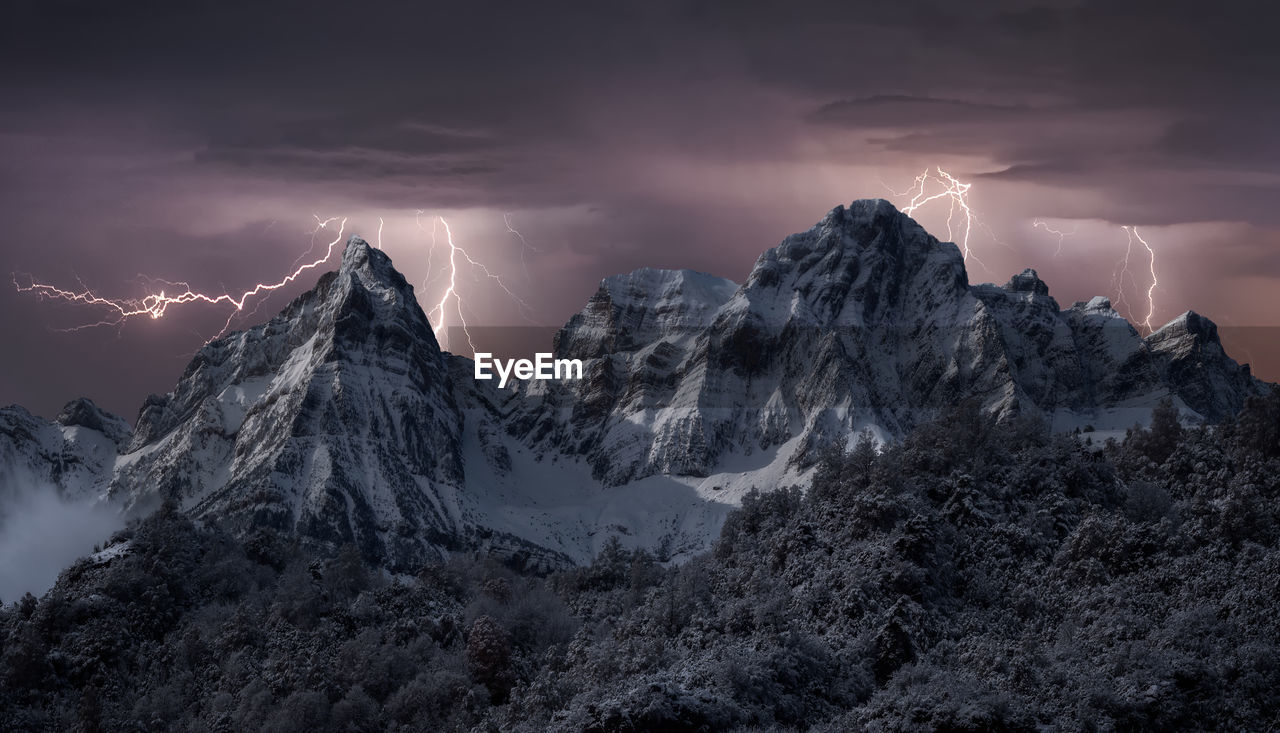 Scenery of mountain range covered with snow under thunderstorm sky with bright lightnings in winter