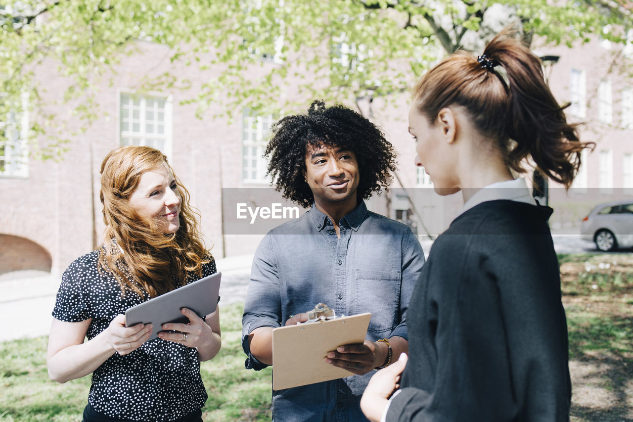 Confident businesswoman discussing with multi-ethnic colleagues while standing outdoors