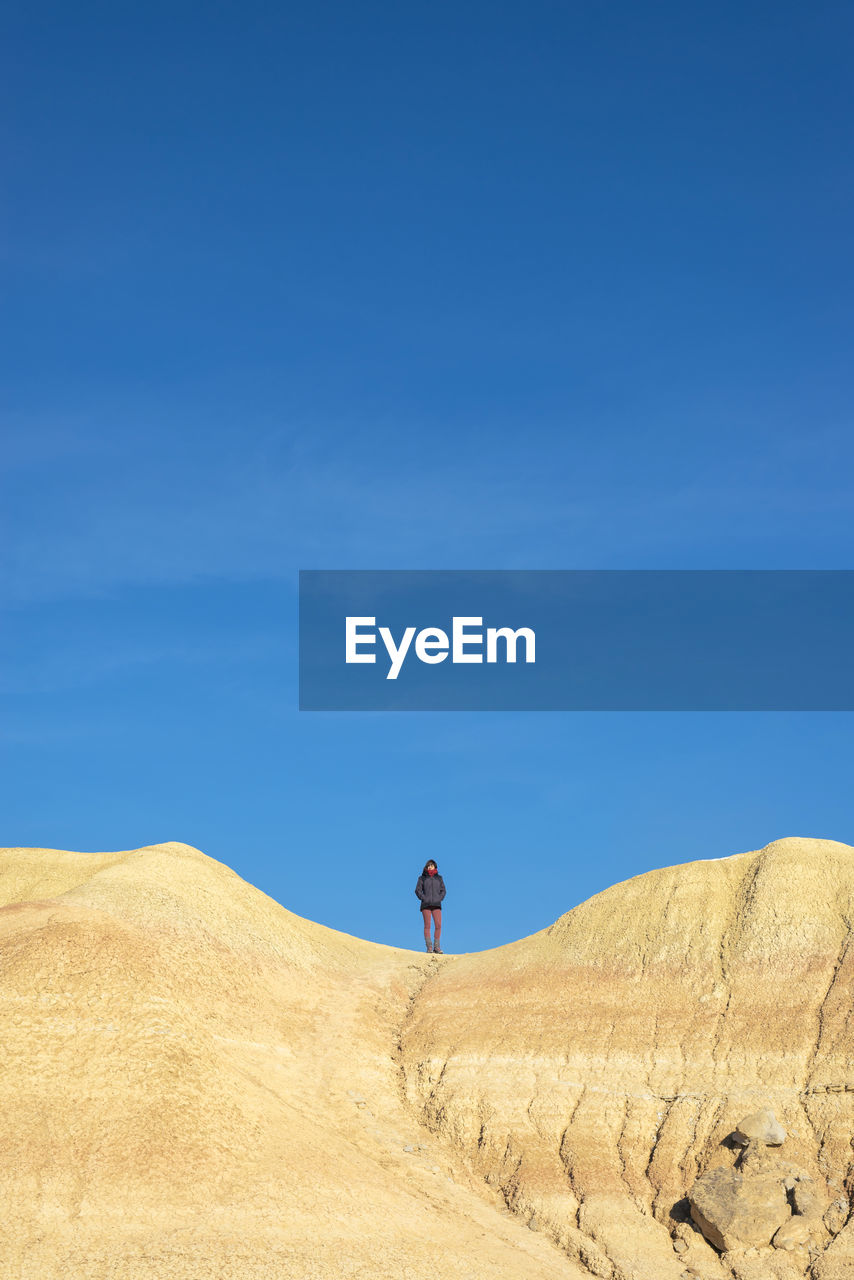 Front view of a woman on top of a hill standing with hands on pocket while looking to horizon