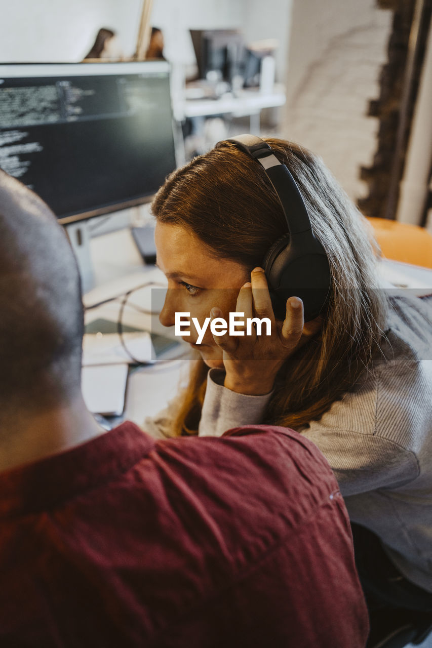 Female programmer listening through headphone while doing coding at startup company