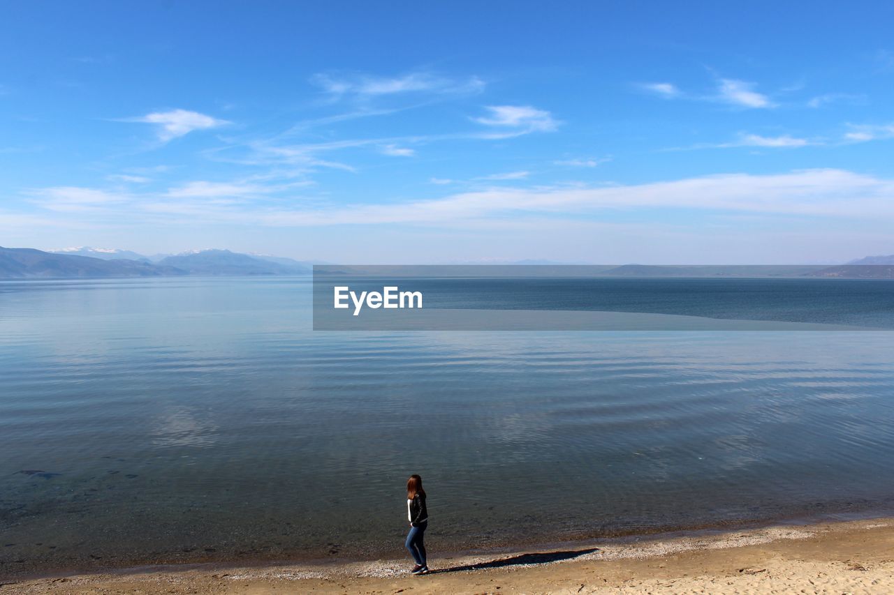 MAN STANDING AT BEACH AGAINST SKY