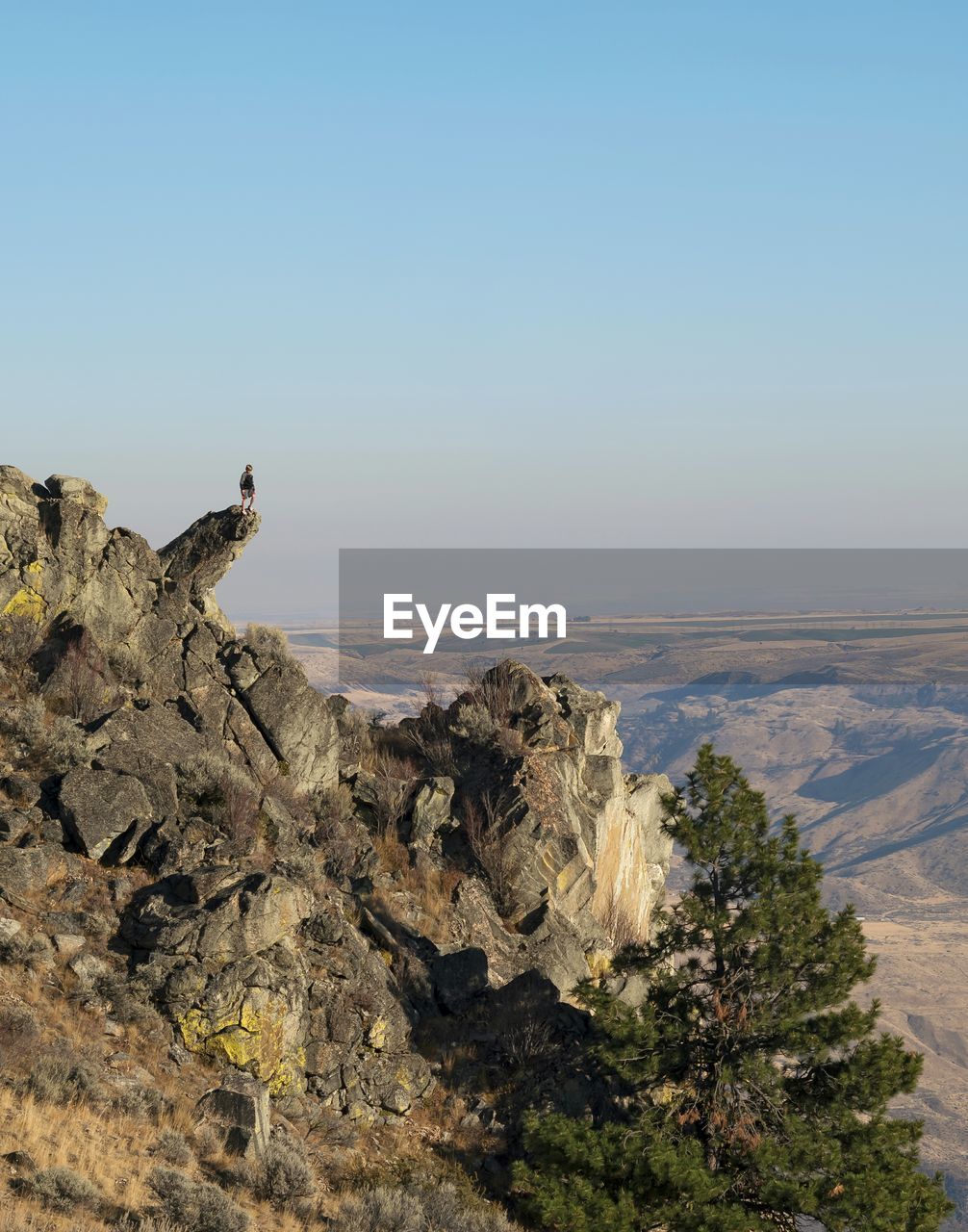 Distant view of boy standing on cliff against clear sky