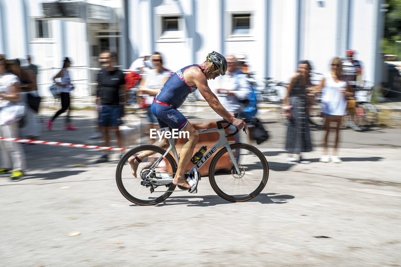 bicycle, transportation, motion, activity, sports, city, architecture, blurred motion, cycling, endurance sports, vehicle, group of people, adult, street, city life, lifestyles, men, road cycling, city street, speed, mode of transportation, sports equipment, building exterior, women, riding, wheel, commuter, footwear, crowd, on the move, built structure, bicycle racing, race, road bicycle racing, full length, road, clothing, cycle sport, person, road bicycle, large group of people, land vehicle, travel, young adult, bicycle wheel, outdoors, exercising, leisure activity, racing bicycle, recreation, day