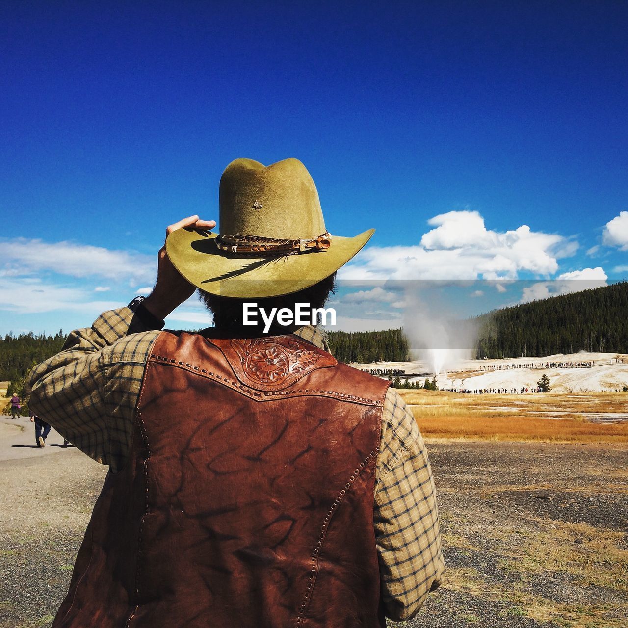 Rear view of cowboy on field against blue sky