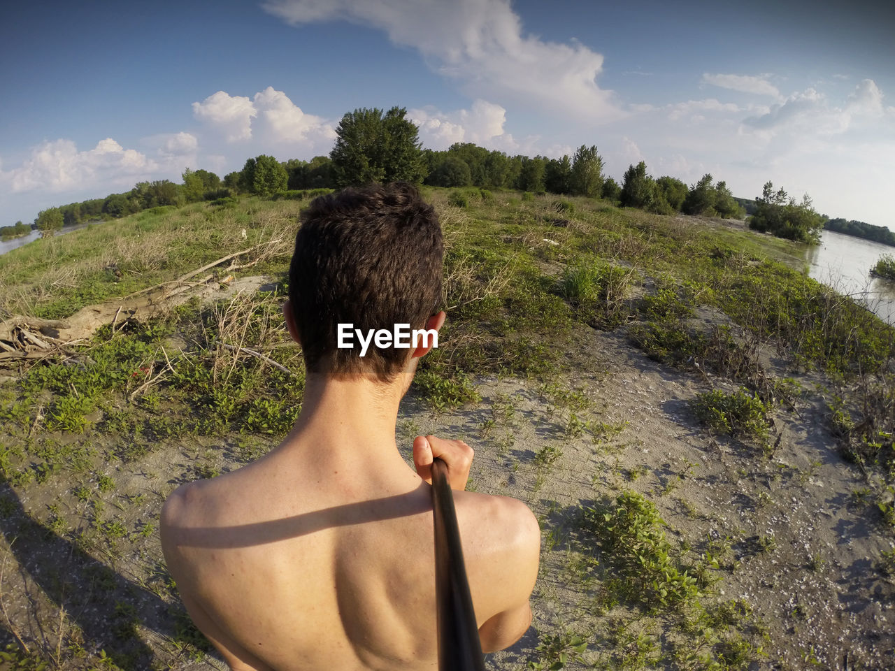 Rear view of shirtless man taking selfie on grassy field against sky