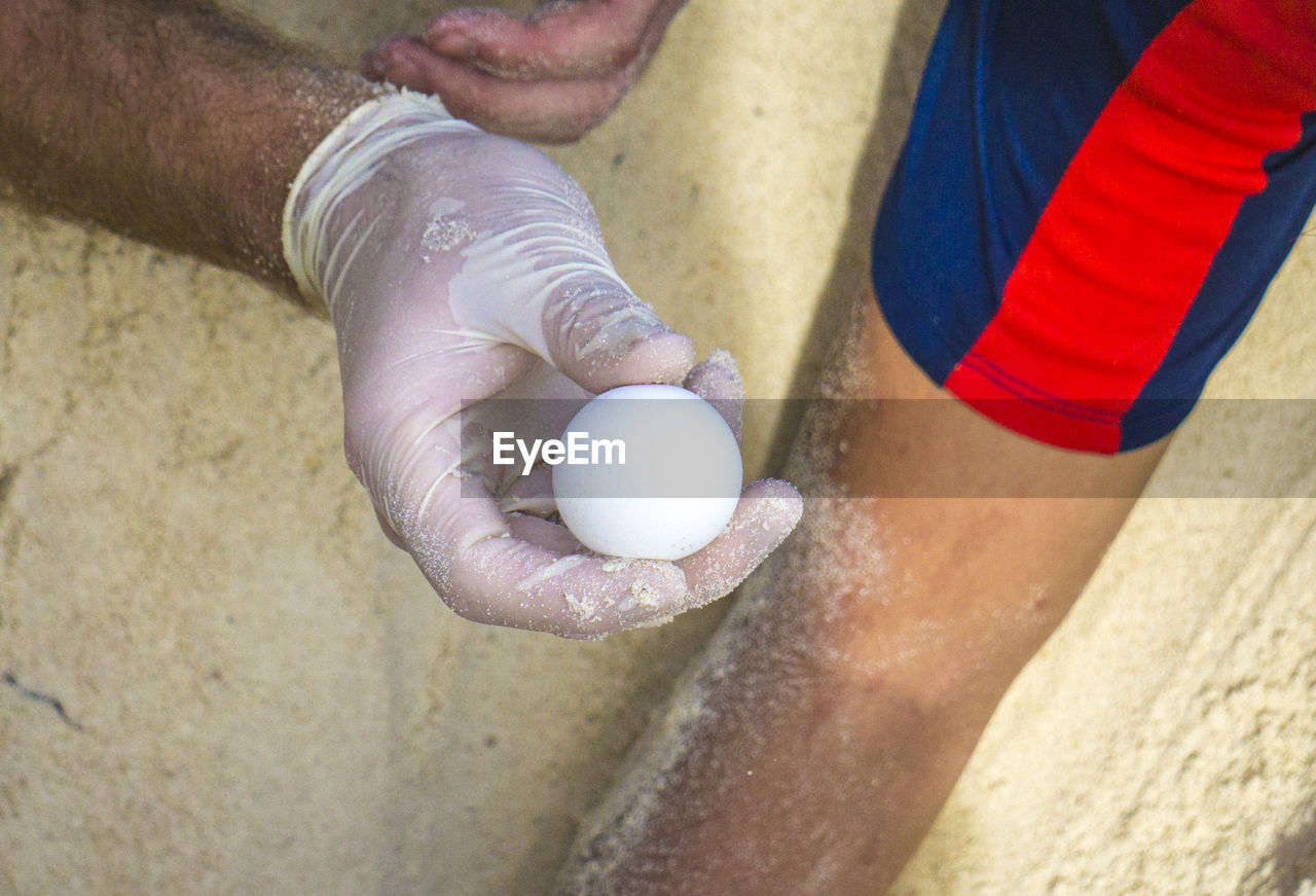 CLOSE-UP OF HAND HOLDING BALL ON BEACH