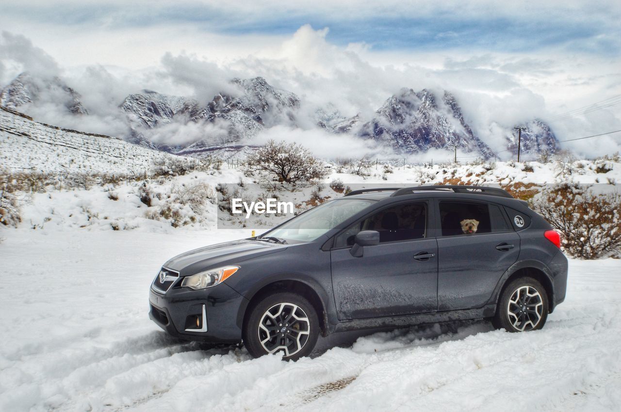 CAR ON SNOW COVERED LAND AGAINST MOUNTAIN