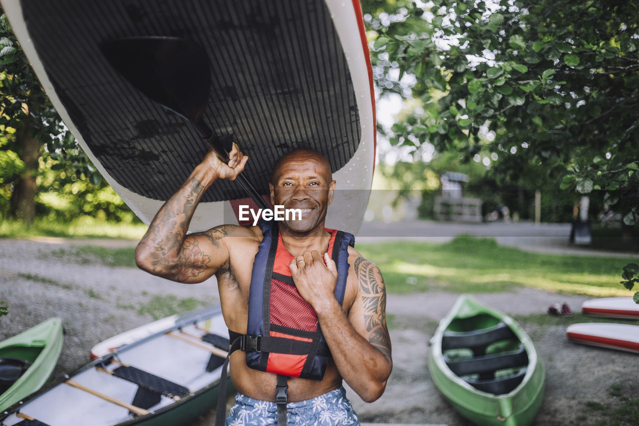 Portrait of smiling man carrying paddleboard and oar