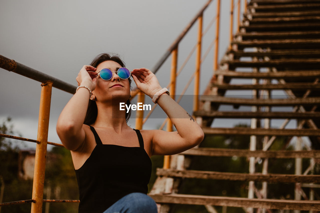 Young woman in sunglasses sitting against steps