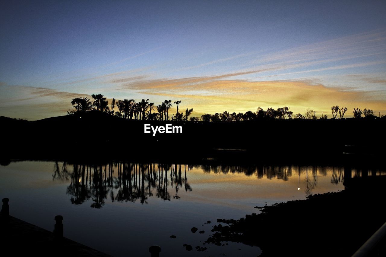 SILHOUETTE TREES BY LAKE AGAINST SKY AT SUNSET