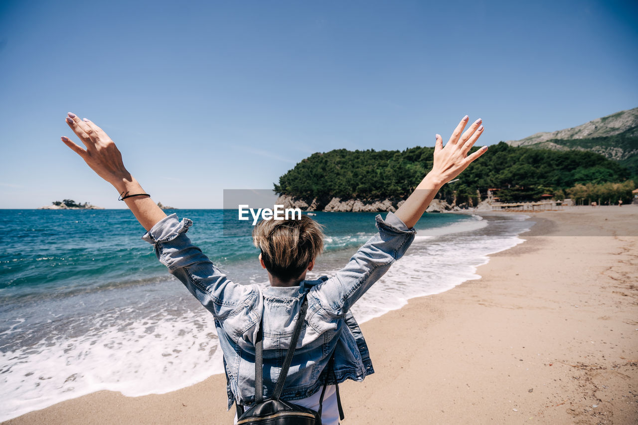 Girl with backpack on beach hands up person