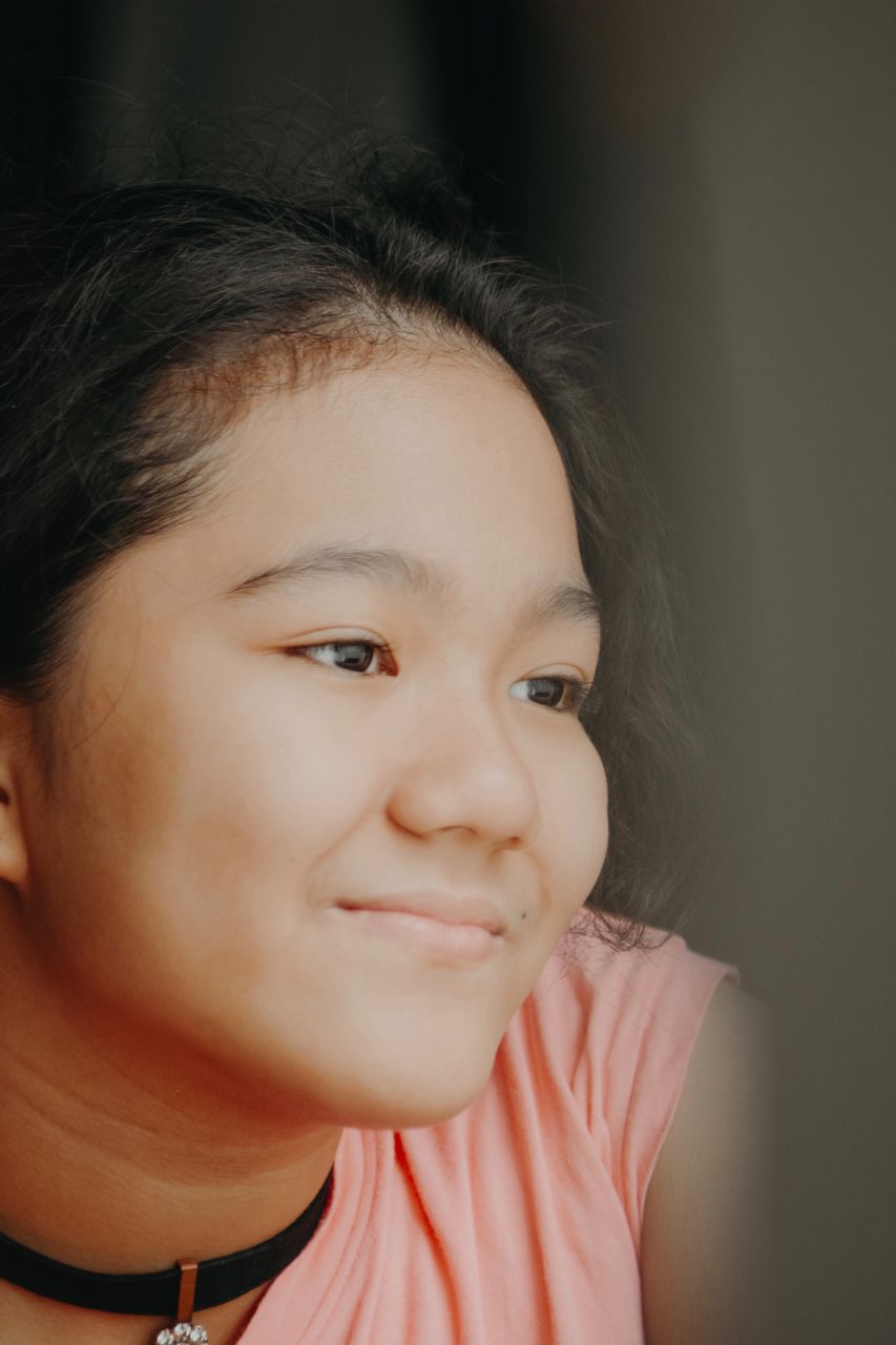 A young girl wearing pink shirt and a choker necklace looking away from the camera 