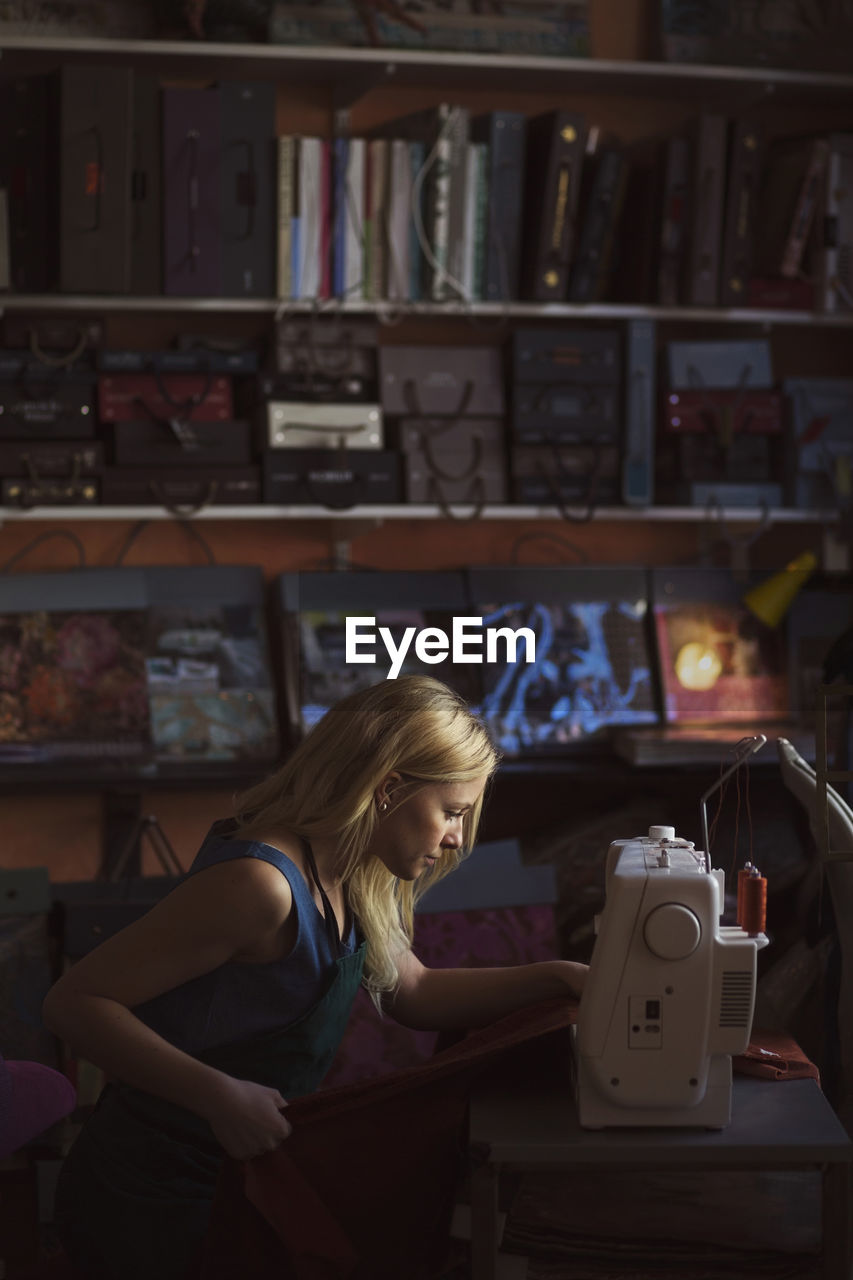 Side view of young female fashion designer using sewing machine in studio