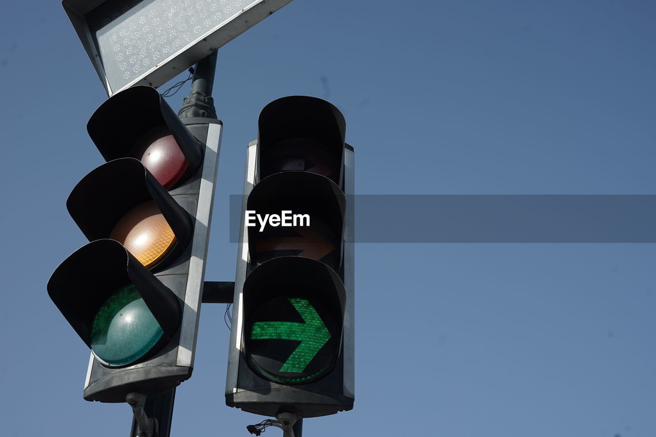 stoplight, signaling device, sign, green light, light, traffic light, road signal, road, guidance, road sign, traffic, light fixture, red light, transportation, communication, illuminated, city, symbol, green, street, lighting equipment, sky, no people, lighting, blue, crossroad, clear sky, control, nature, warning sign, road intersection, architecture, street light, light - natural phenomenon, outdoors, low angle view, directional sign, city life, crosswalk, security, day, crossing, technology, stop sign, protection, authority
