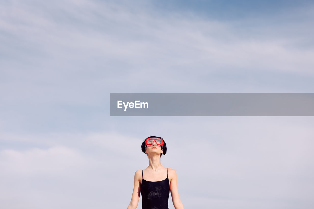 low angle view of woman with arms raised standing against sky